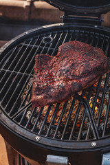 Close up on the blackened and charred bark of a smoked beef brisket, in a slow cooking background