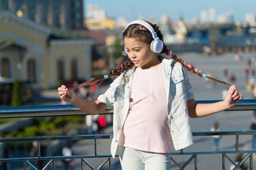 I love my pigtail hairstyle. Small child wearing braided hairstyle and headphones outdoor. Little girl with long hairstyle in casual wear. Cute kid following modern hairstyle and technology trends