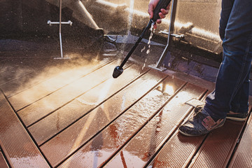man cleaning terrace with a power washer - high water pressure cleaner on wooden terrace surface
