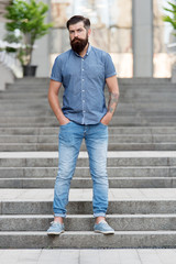 Obraz premium In love with denim. Man bearded hipster fashion model wear denim clothes urban background stairs. Regular walk in city center. Confident guy wear jeans denim trousers and shirt. Comfortable outfit