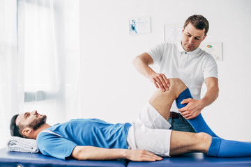 handsome Physiotherapist massaging leg of football player in hospital