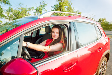 Portrait of smiling business lady, caucasian young woman driver in red clothes looking at camera and smiling while sitting behind the wheel red car. Selective focus, copy space.