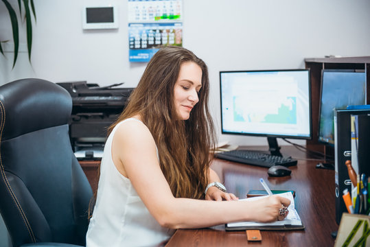 Young caucasian business lady sitting on her workplace in office. Female entrepreneurship. Portrait of skilled manager satisfied with occupation. Selective focus, copy space.