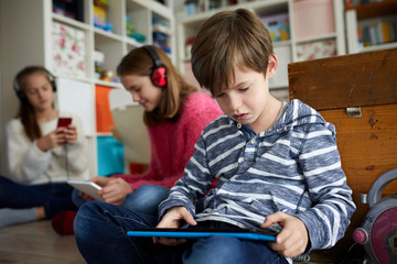 Siblings playing at home with their digital tablets, sitting on ground