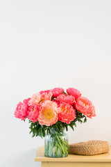 Coral peonies in a glass vase and wicker bag on wooden table.. Beautiful peony flower for catalog or online store. Floral shop concept . Beautiful fresh cut bouquet. Flowers delivery. Copy space