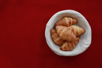 Five freshly baked tasty crusty croissants in a basket on red tablecloth .