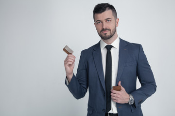 Portrait of young attractive businessman with serious and confident look, holding wooden comb....