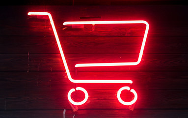 Red neon shopping cart on wooden surface at night