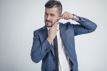 Barbershop advertising concept. Businessman with serious face isolated on white background. Man with beard holds razor. Macho in formal suit shaves beard and moustache.