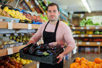 Salesman having tray of  eggplants on the supermarket