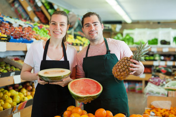 Young man and woman wearing aprons offering fresh fruits