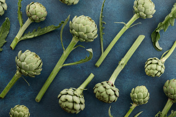 Fresh green artichoke with stem and leaves on aquamarine background, top view