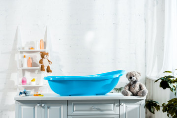 blue baby bathtub near teddy bear and baby sneakers in bathroom