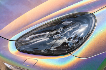 Close-up LED headlight expensive car part with exclusive iridescent painting. Vehicle covered with...