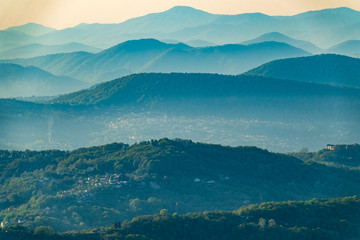 Naklejka premium Layers of mountains in the haze during sunset. Beautiful sunset in the mountains. Beautiful sunset in a hilly valley with villages and fog in the lowlands.
