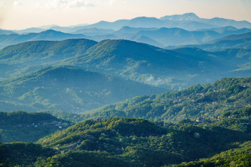 Obraz premium Layers of mountains in the haze during sunset. Beautiful sunset in the mountains. Beautiful sunset in a hilly valley with villages and fog in the lowlands.