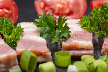 Uncured Apple Smoked Bacon, Red Tomatoes, fresh Curly Parsley and Green Onion Scallions arranged on natural black stone background. 