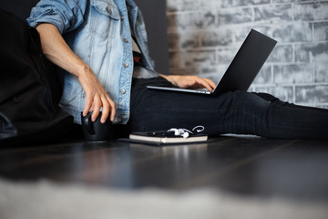 young man in denim jacket and black cap sitting on the floor working on laptop