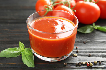 Glass of tomato sauce with basil on wooden table, closeup