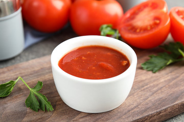 Wooden board with bowl of tomato sauce and parsley on table