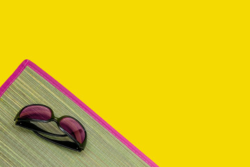 Sunglasses on a wicker bast beach mat with pink edging on a yellow background. Hot summer and beach...