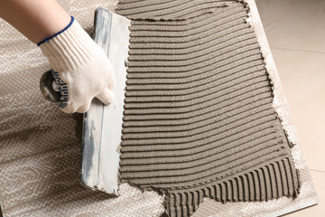 Worker spreading concrete on ceramic tile with spatula, closeup. Space for text