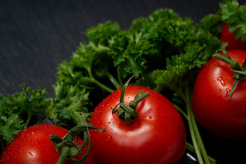 Organic Red Tomatoes on the vine and fresh Curly Parsley arranged on natural stone background....