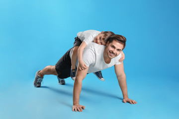 Dad doing push-ups with son on his back against color background