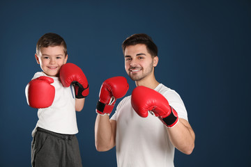 Fototapeta na wymiar Dad and his son with boxing gloves on color background