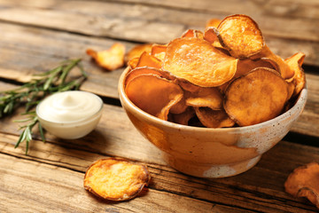 Delicious sweet potato chips in bowl, rosemary and sauce on table. Space for text