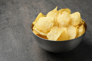Delicious crispy potato chips in bowl on table, space for text