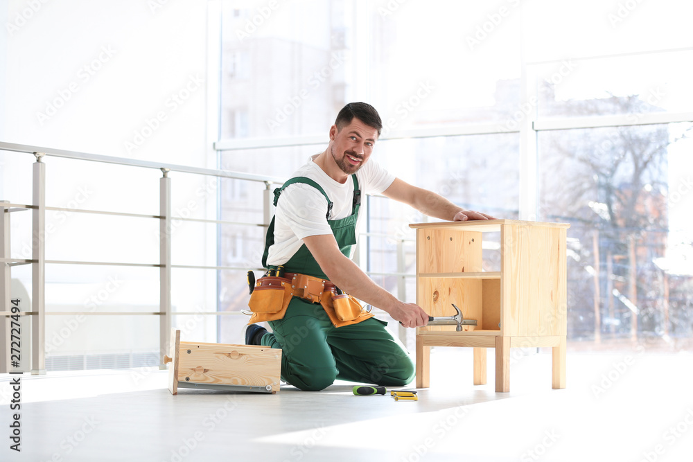 Wall mural Handyman in uniform assembling furniture indoors. Professional construction tools