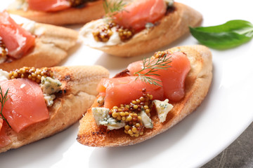 Tasty bruschettas with salmon and blue cheese on plate, closeup
