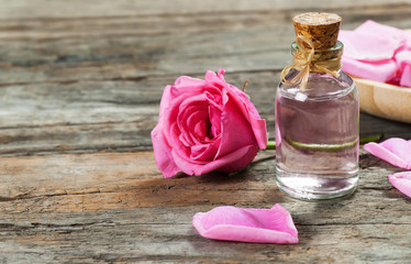 Obraz na płótnie Canvas pink rose flower and glass of bottle essential oil or rose water with rose petals, spa and aromatherapy cosmetic concept