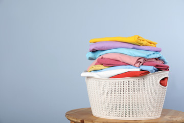 Plastic laundry basket with clean clothes on stool against color background. Space for text