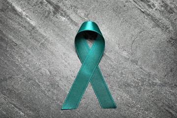 Teal ribbon on grey background, top view