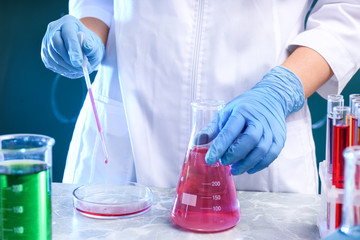 Scientist taking sample of liquid with dropper at table, closeup. Chemistry glassware