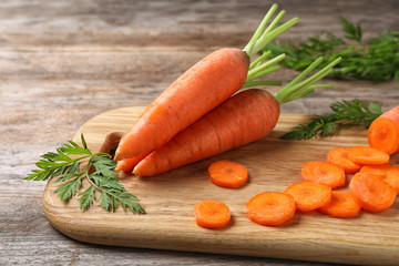Board with cut carrot on wooden background