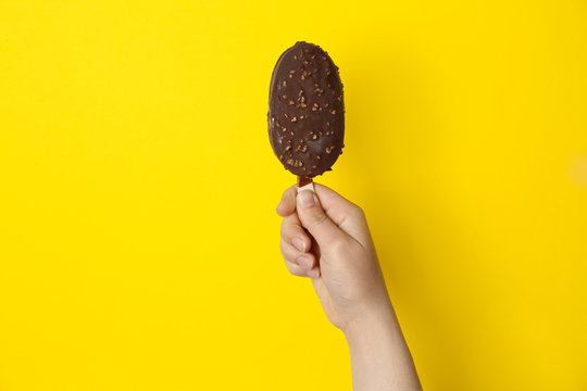 Woman holding delicious ice cream with chocolate against color background