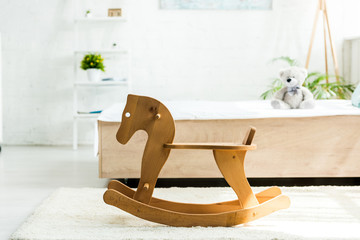 Fototapeta na wymiar selective focus of wooden rocking horse near bed with white bedding and teddy bear