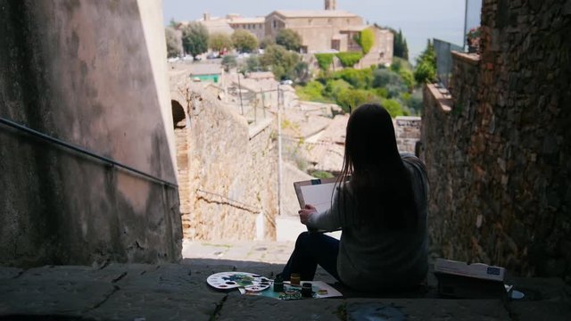 A young attractive woman is sitting on a staircase drawing a house.