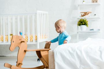 adorable toddler child standing near wooden rocking horse in modern bedroom