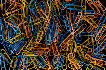 top view of scattered yellow, orange and blue paper clips isolated on black