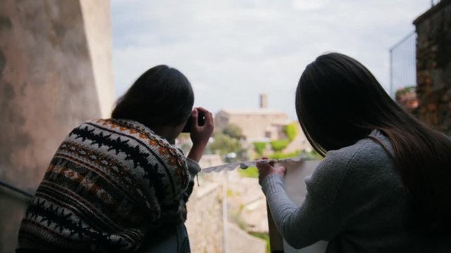 Two women sit by the stairs one of them draws. Then another woman gets a photo camera.