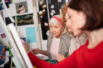 Aged grey-haired artist looking at works of her students