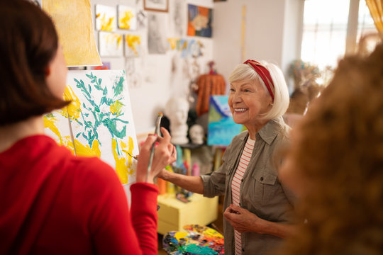 Cheerful retired woman teaching her students to paint