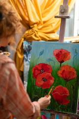 Curly red-haired artist standing near canvas with red poppies