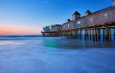 The Pier at Old Orchard Beach of Maine before sunrise. The wooden pier on the beach contains many other tourist businesses, including a variety of souvenir shops.