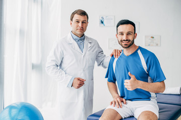 smiling Physiotherapist near football player showing thumb up in hospital
