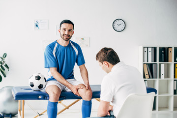 Physiotherapist examining smiling football player in hospital